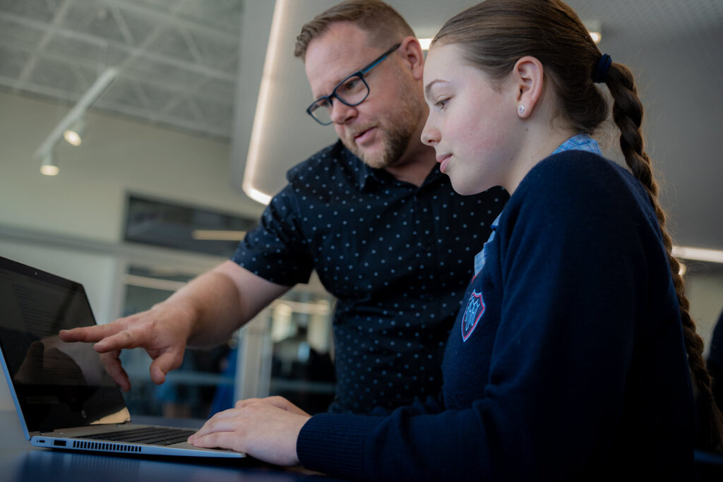 Un profesor ayudando a una estudiante que trabaja con EdChat en una computadora.