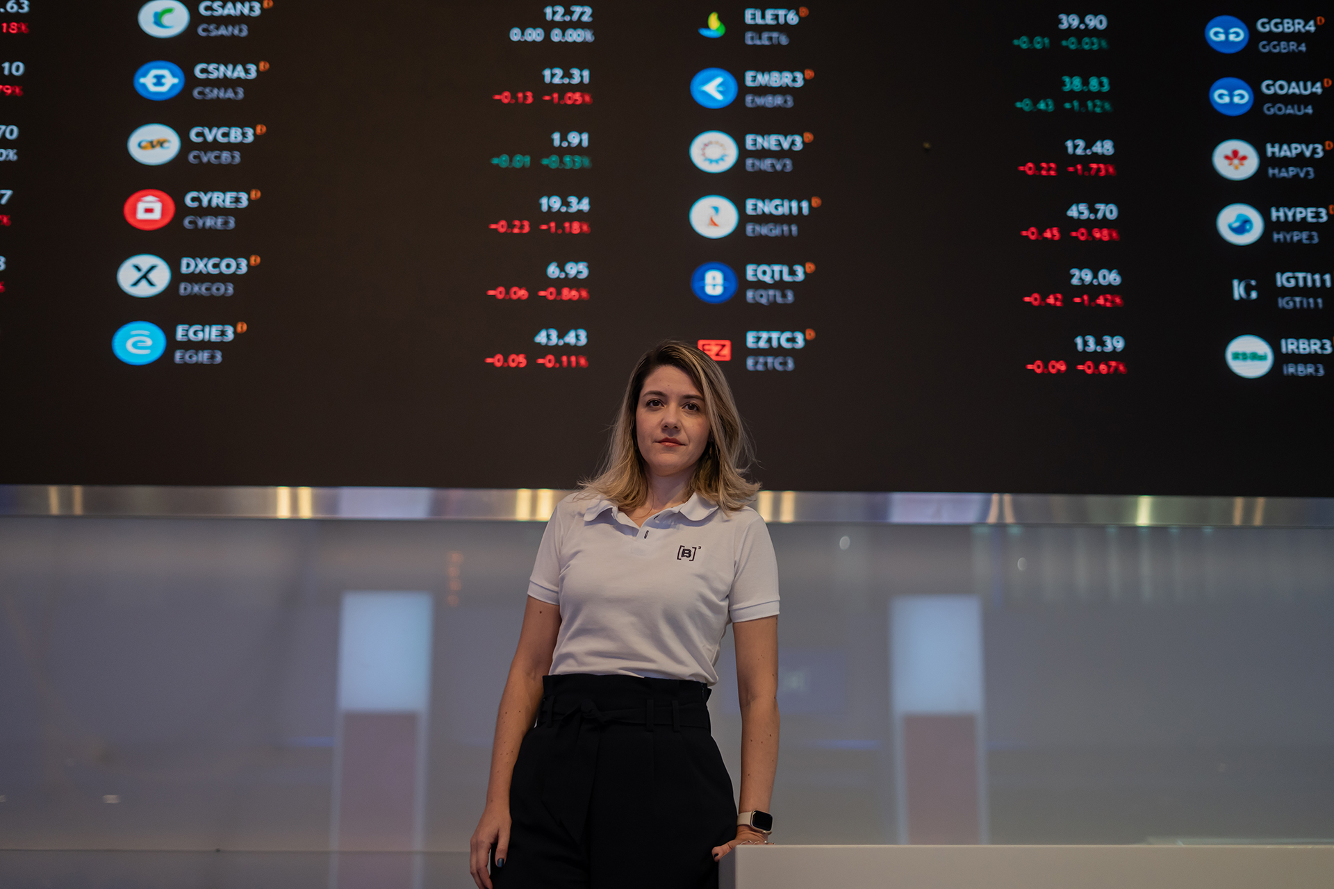 Christianne Bariquelli parada frente a una pantalla negra gigante que muestra símbolos de teletipo en colores vivos.