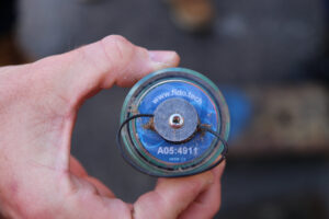 Close de uma mão segurando um sensor FIDO azul, com um elástico para prendê-lo aos canos.
