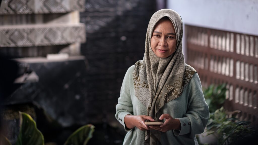 Ira Nasihatul Husna, uma criadora de tilápias, usa um copiloto em seu celular para verificar os horários de alimentação e a qualidade da água em sua fazenda de tilápias. Foto de Fauzy Chaniago para a Microsoft.