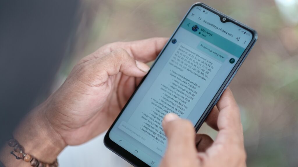 O criador de camarão Andriyono verifica o copiloto Mas Ahya no aplicativo eFarm da eFishery para uma análise da água em seus lagos. Foto de Fauzy Chaniago para a Microsoft.