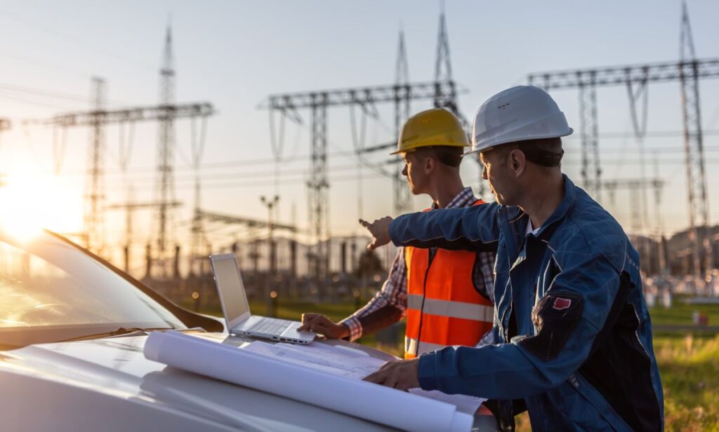 Hombres con cascos para construcción y chalecos observan una laptop