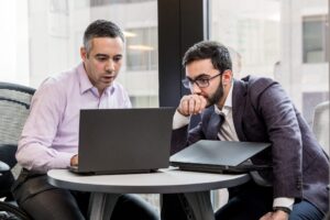 dois homens de terno olham para um computador
