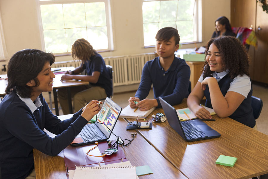 Tres estudiantes en una mesa con laptops que muestran Microsoft MakeCode