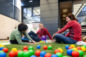 Un hombre, una mujer y un niño sentados en jardín, rodeados por pelotas de plástico de colores