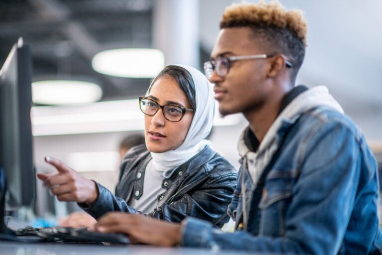Dos estudiantes de educación superior sentados en un escritorio, trabajan en una computadora