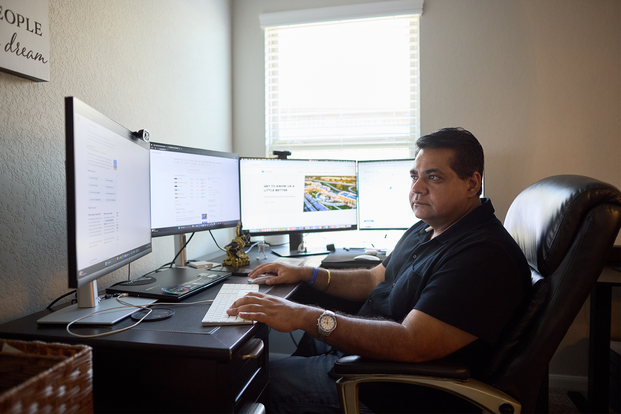 Un hombre con playera negra escribe en un teclado en un escritorio con cuatro monitores