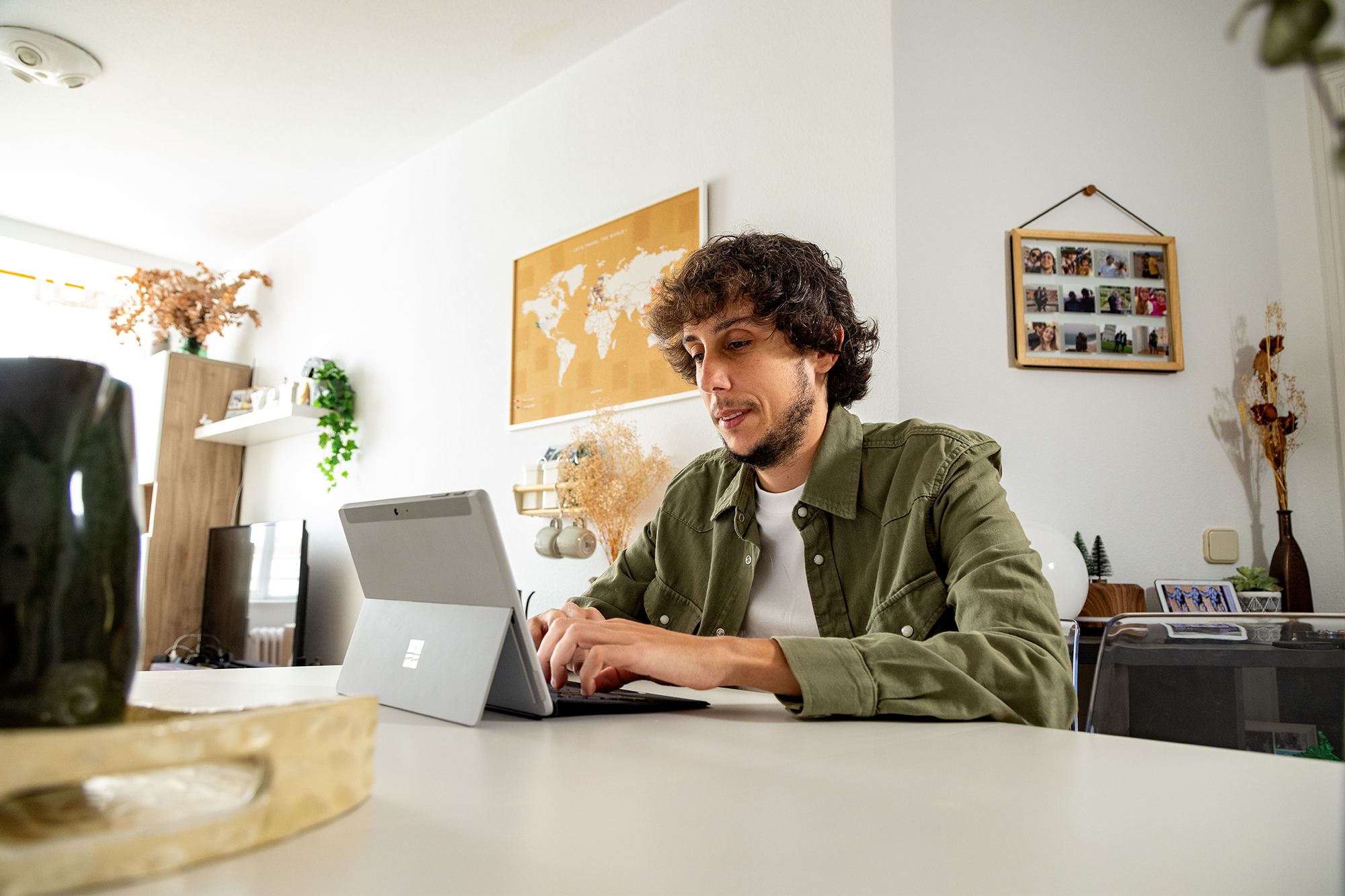 Un hombre con cabello negro rizado y barba corta, con una camisa khaki abierta, trabaja en una laptop