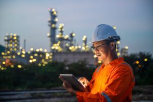 Un ingeniero con casco de seguridad utiliza una tableta digital mientras trabaja en el turno nocturno en una refinería de petróleo