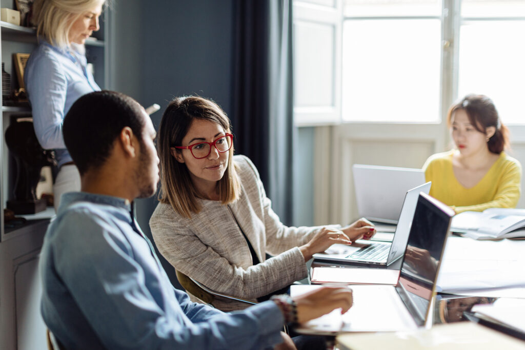 Cuatro personas en una oficina trabajan en diferentes dispositivos