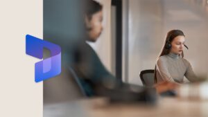Dos compañeros de trabajo sentados uno junto al otro en una mesa de sala de conferencias. Hay un borde grueso de color beige en el lado izquierdo de la imagen, con el logotipo de Dynamics 365 superpuesto.