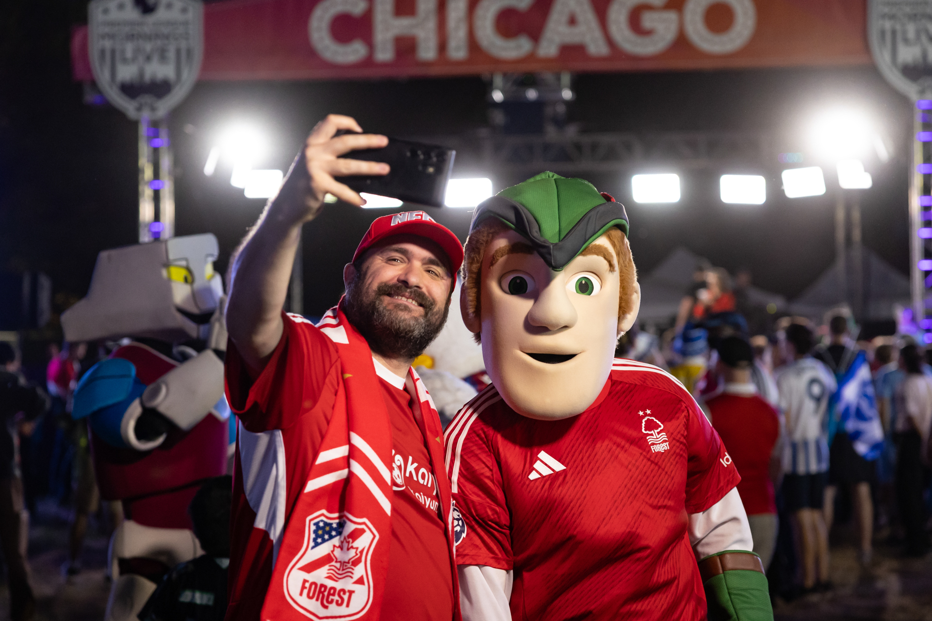 Un hombre con un jersey de Nottingham Forest posa con la mascota del equipo con una bandera que dice Chicago al fondo