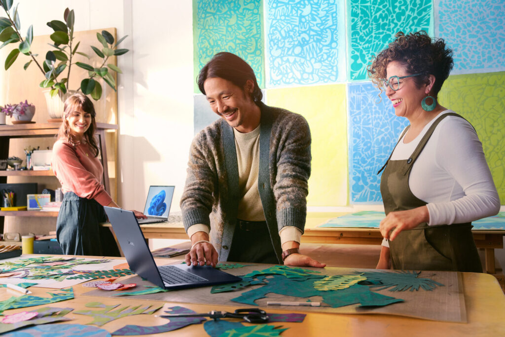 Tres personas sonríen mientras trabajan con laptops en un estudio creativo